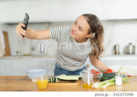 Teenage girl looking at smartphone and preparing salad Teenage girl looking at smartphone and preparing salad 142255096