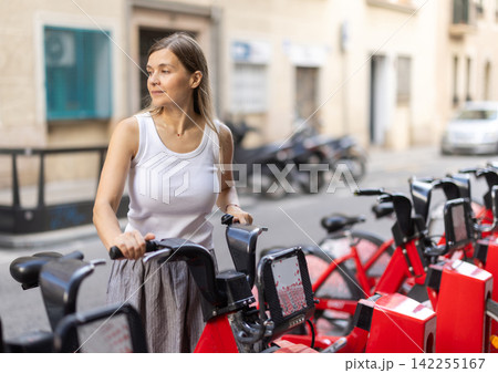 Woman rents bicycle, starts journey at parking lot Woman rents bicycle, starts journey at parking lot 142255167