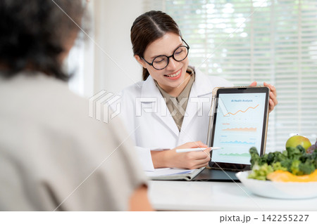 Asian nutritionist showing AI health analysis graph on tablet to senior patient. Asian nutritionist showing AI health analysis graph on tablet to senior patient. 142255227
