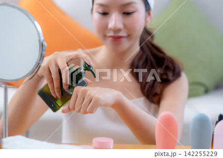 Beautiful young asian woman applying lotion herb on hands looking mirror at home. Beautiful young asian woman applying lotion herb on hands looking mirror at home. 142255229