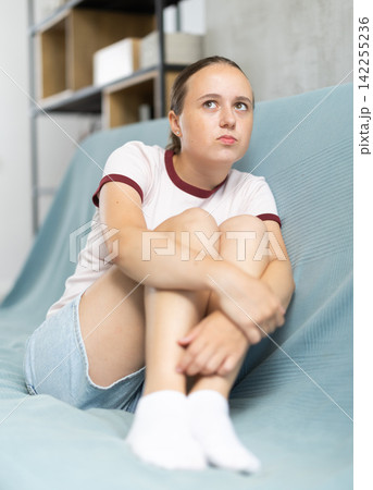 Uupset girl is sitting on couch in her room. She thinking and worrying about something 142255236