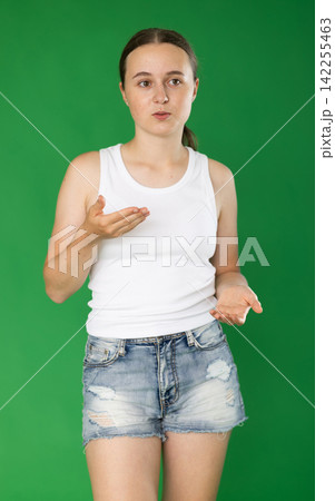 Teenage girl in denim skirt explains and tells something against green background Teenage girl in denim skirt explains and tells something against green background 142255463