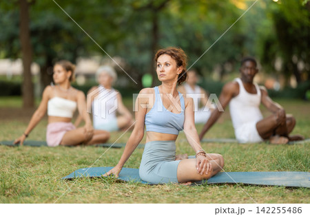 Woman stretching in lotus position during group yoga in park Woman stretching in lotus position during group yoga in park 142255486