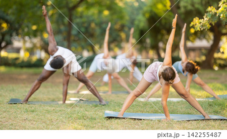 Multinational yoga enthusiasts with female coach perform Prasarita Padottanasana in park Multinational yoga enthusiasts with female coach perform Prasarita Padottanasana in park 142255487