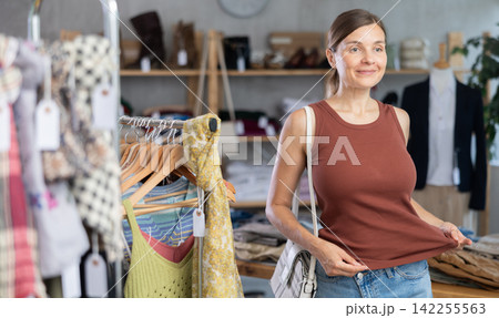 Adult woman trying on brown tank top in store 142255563