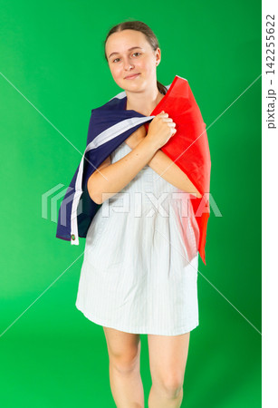 Teen girl dressed in summer dress posing against green background waving France flag 142255622