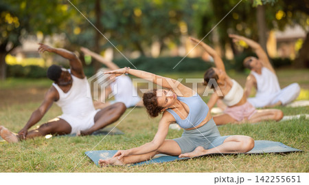 Multinational yoga enthusiasts with female coach perform Janu Shirshasana in park 142255651