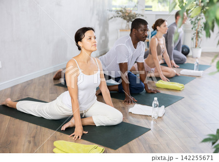 Young woman maintaining mental and physical health attending multinational group yoga class at studio, practicing twisting poses 142255671