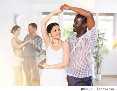 Positive woman and African american man practicing bachata dance moves in pair during group class 142255738
