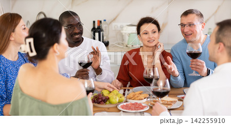 Happy adult friends at the festive table discussing news and drinking red wine Happy adult friends at the festive table discussing news and drinking red wine 142255910