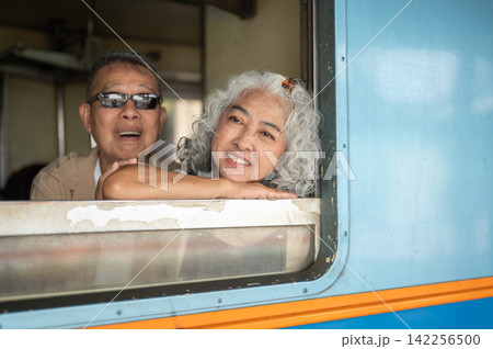 Asian senior elderly couple smiling and posing over train window and enjoying a joyful travel moment Asian senior elderly couple smiling and posing over train window and enjoying a joyful travel moment 142256500