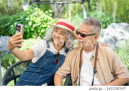 Asian senior elderly couple taking a selfie together with smartphone during a relaxing garden visit. Asian senior elderly couple taking a selfie together with smartphone during a relaxing garden visit. 142256547