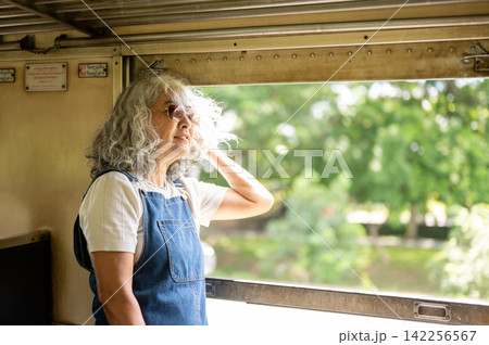 Asian senior woman enjoying a peaceful train journey while looking through the window Asian senior woman enjoying a peaceful train journey while looking through the window 142256567