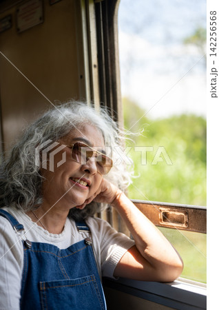 Asian senior elderly woman enjoying the scenery from a vintage train window during a solo trip. Asian senior elderly woman enjoying the scenery from a vintage train window during a solo trip. 142256568