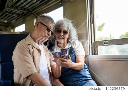 Asian senior elderly couple looking at smartphone together while enjoying their vintage train trip. Asian senior elderly couple looking at smartphone together while enjoying their vintage train trip. 142256579