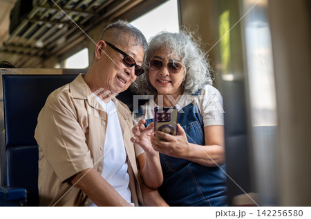 Asian senior couple looking at photos on a smartphone while traveling by train 142256580