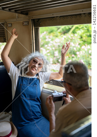 Asian senior woman photographing scenery from a train window during a joyful journey Asian senior woman photographing scenery from a train window during a joyful journey 142256681