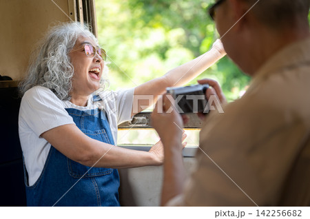 Asian senior woman laughing while photographing scenery during a train journey Asian senior woman laughing while photographing scenery during a train journey 142256682