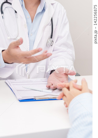 Doctor and patient having a medical consultation in a hospital room, explaining a treatment plan, discussing diagnosis, and giving advice during a medical health checkup appointment in a clinic 142256875