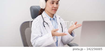 Professional doctor wearing headphone and lab coat using laptop for telehealth, telemedicine, online consultation and medical technology video meeting at desk in hospital office concept Professional doctor wearing headphone and lab coat using laptop for telehealth, telemedicine, online consultation and medical technology video meeting at desk in hospital office concept 142256885