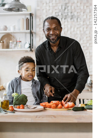 A father and his young son are happily preparing vegetables in a bright, modern kitchen, fostering a sense of togetherness and healthy eating 142257364