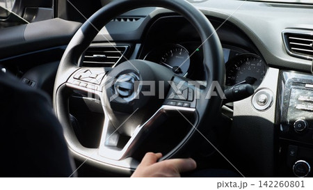Male arms holds steering wheel while driving a motor car at city. Young man operating the automobile at urban road. Driver moving in his auto on route. Slow motion 142260801