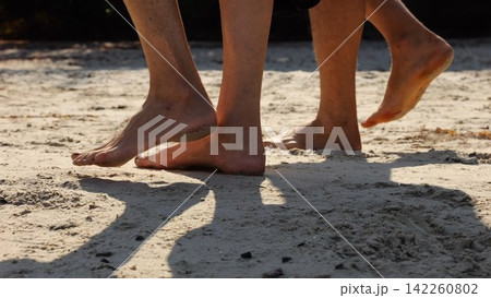Male and female legs of pair walking on sandy beach. Bare feet of couple stepping along sand shore at sunny day. Lovers spending time together at resort. Concept of summer vacation or holiday Male and female legs of pair walking on sandy beach. Bare feet of couple stepping along sand shore at sunny day. Lovers spending time together at resort. Concept of summer vacation or holiday 142260802