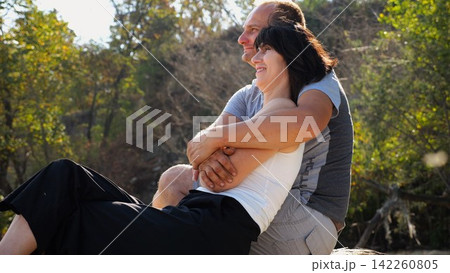 Happy pair hugs during sitting on wooden log on beach. Romantic couple admiring sea landscape at sunny day. Lovers spending time together at resort. Concept of summer vacation or holiday. Slow mo Happy pair hugs during sitting on wooden log on beach. Romantic couple admiring sea landscape at sunny day. Lovers spending time together at resort. Concept of summer vacation or holiday. Slow mo 142260805