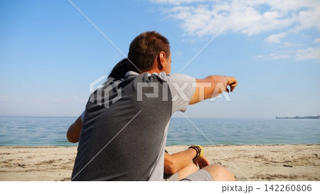 Happy pair hugs during sitting on wooden log on beach. Romantic couple admiring sea landscape at sunny day. Lovers spending time together at resort. Concept of summer vacation or holiday. Slow mo Happy pair hugs during sitting on wooden log on beach. Romantic couple admiring sea landscape at sunny day. Lovers spending time together at resort. Concept of summer vacation or holiday. Slow mo 142260806