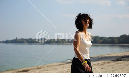 Beautiful lady walking on sandy beach near shoreline at sunny day. Happy adult woman turning around near coastline. Carefree female enjoying rest at seaside. Concept of summer vacation or holiday Beautiful lady walking on sandy beach near shoreline at sunny day. Happy adult woman turning around near coastline. Carefree female enjoying rest at seaside. Concept of summer vacation or holiday 142260807