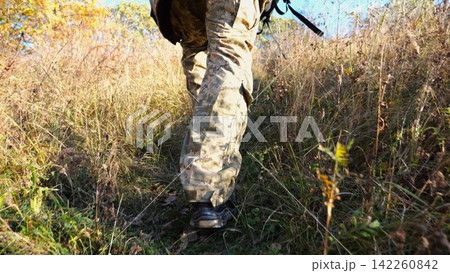 Low view to male feet of ukrainian soldiers going along trail at countryside. Legs of young army man walking through dry grass at sunny day. War in Ukraine. Slow motion 142260842