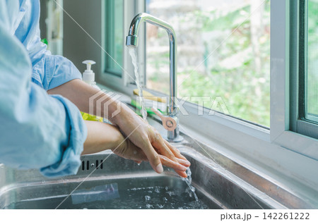 Asian hand woman wearing blue shirt washing both hands. clean your finger with water and foam soap in the kitchen sink before eating. concept germ safety Asian hand woman wearing blue shirt washing both hands. clean your finger with water and foam soap in the kitchen sink before eating. concept germ safety 142261222