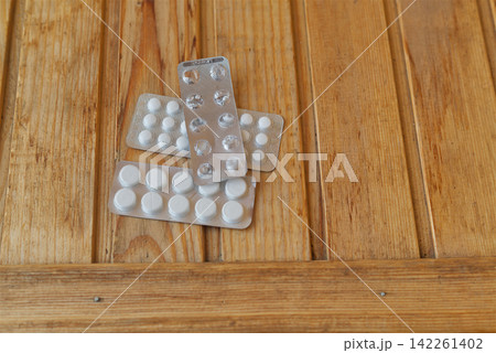 Close-up of a used empty blister lying on new packs of white pills on a rough wooden table 142261402