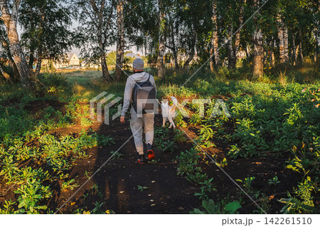 Man walking with white dog on forest trail. 142261510