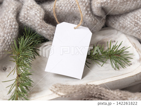 Vertical gift tag mockup near beige knitted blanket and fir branches. Rustic Christmas packaging Vertical gift tag mockup near beige knitted blanket and fir branches. Rustic Christmas packaging 142261822