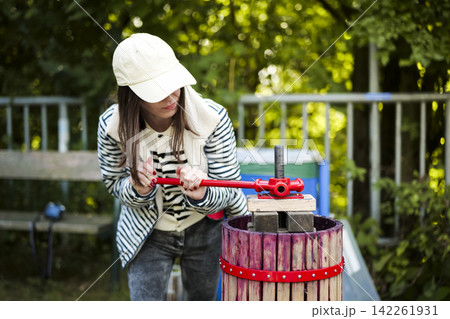 Woman turning a manual fruit press with visible effort during a sustainable winemaking workshop, highlight regional techniques. 142261931
