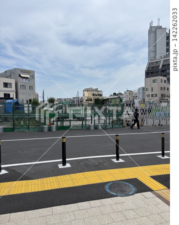 アスファルト道路と仮設フェンスが続く、昼下がりの街並み 142262033