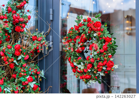 a festive red rose wreath hanging on a doorway with green leaves and twine, creating a warm holiday decoration for home decor a festive red rose wreath hanging on a doorway with green leaves and twine, creating a warm holiday decoration for home decor 142263027