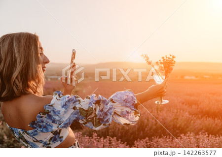 Woman lavender smartphone taking photo of glass with flowers in a field during sunset golden hour Woman lavender smartphone taking photo of glass with flowers in a field during sunset golden hour 142263577