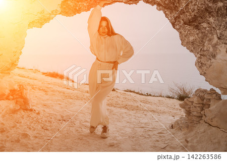 Woman cave sunset posing at the entrance of a coastal cavern during golden hour with a view of the sea Woman cave sunset posing at the entrance of a coastal cavern during golden hour with a view of the sea 142263586