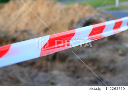 Close-up of striped warning ribbon blocking access to an underground pipeline repair pit. Concept of site security, danger warnings 142263860
