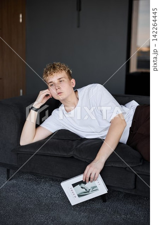 Contemplative caucasian student lounging with magazine 142264445