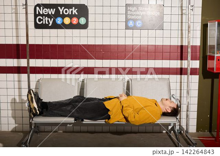 Individual relaxes on subway bench amidst lively city advertisements Individual relaxes on subway bench amidst lively city advertisements 142264843