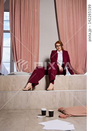 Cultivated woman in deep red scrutinizes sketches meticulously Cultivated woman in deep red scrutinizes sketches meticulously 142265199