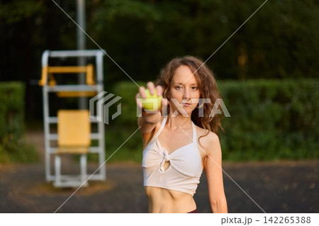 Sunset park setting with woman holding tennis ball confidently 142265388
