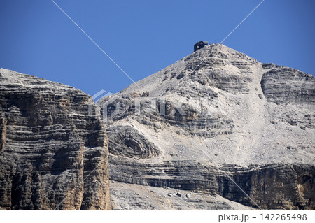 hiking trail to Pordoi massif in the Dolomites rocky cliffs, as seen from the high-altitude green meadows near the famous Viel dal Pan Trail. hiking trail to Pordoi massif in the Dolomites rocky cliffs, as seen from the high-altitude green meadows near the famous Viel dal Pan Trail. 142265498