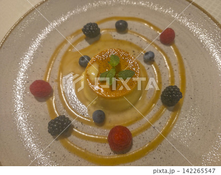 Creamy caramel flan plated with concentric caramel sauce rings, fresh raspberries, blackberries and blueberries, topped with mint leaves; an elegant, ideal for restaurant menus or food blogs. 142265547