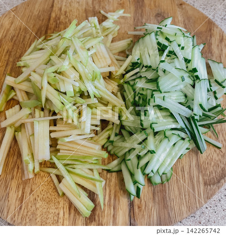 Julienne cut green apple and fresh cucumber matchsticks side by side on round wooden chopping board at home kitchen stock photo 142265742