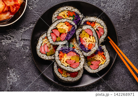 A black plate filled with kimbap (or gimbap) that have colorful fillings. 142268971