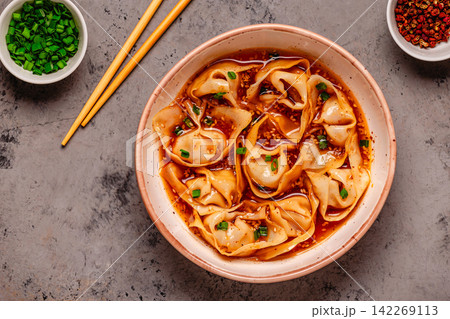 Wontons are placed in a bowl with spicy sauce. Wontons are placed in a bowl with spicy sauce. 142269113